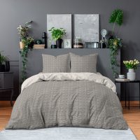 Double bed with floral bedding and dark blankets standing in grey bedroom interior with fresh plants, paintings and lamp